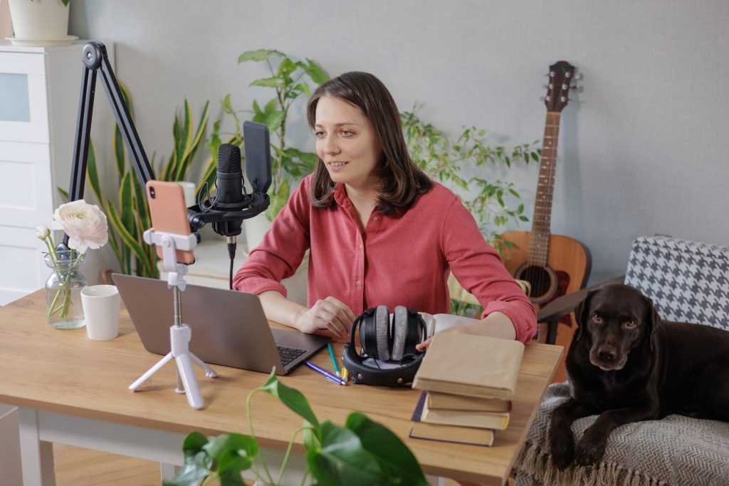 woman in a home office records podcast audio content with a microphone and headphones and a labrador